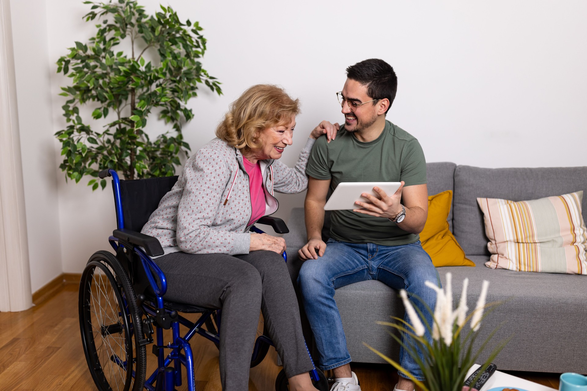 Older woman in wheelchair with man using tablet device.